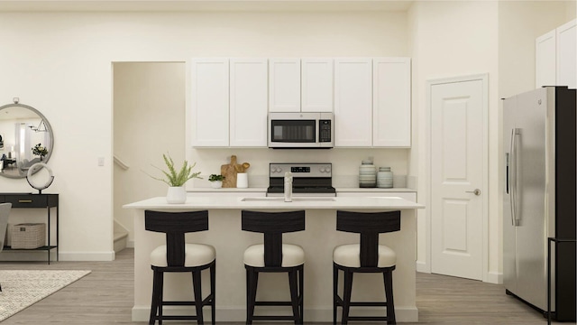kitchen featuring stainless steel appliances, light wood-style flooring, a kitchen bar, and white cabinets