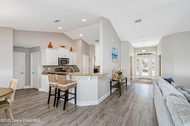 4569 Lady Hawk Way, Melbourne, FL 32904 - kitchen featuring appliances with stainless steel finishes, a breakfast bar, vaulted ceiling, light wood-style floors, and white cabinets