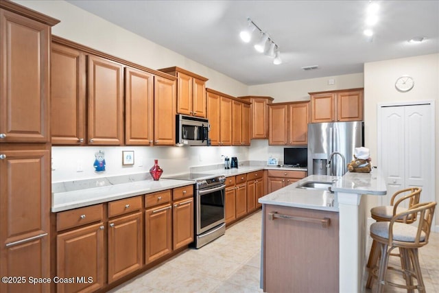 kitchen featuring a breakfast bar area, brown cabinets, a sink, stainless steel appliances, and light countertops