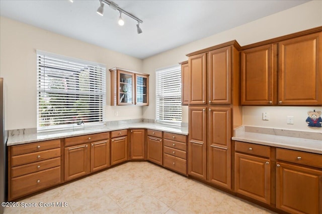 kitchen featuring rail lighting, light stone counters, glass insert cabinets, and brown cabinets