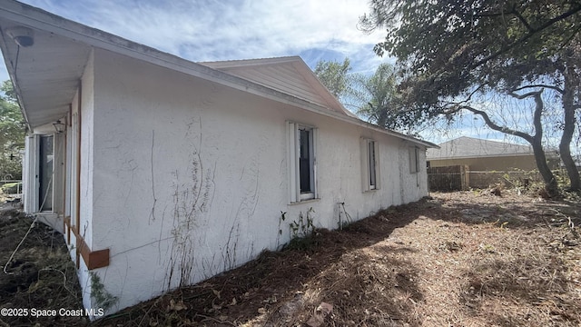 view of side of property with stucco siding and fence