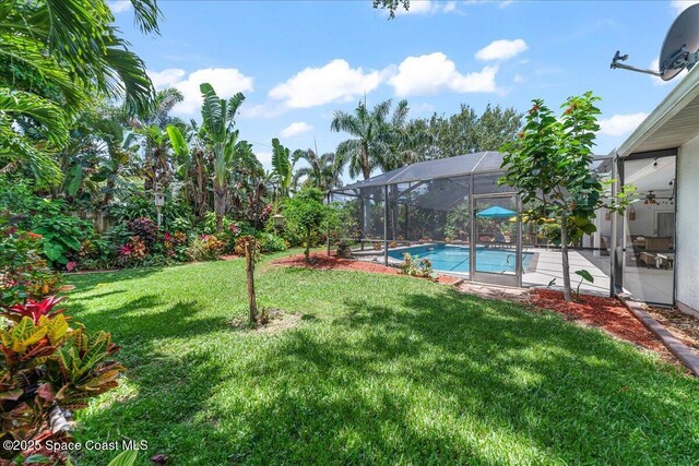 1085 Mercedes Dr, Merritt Island, FL 32952 - view of grassy yard featuring a ceiling fan, an outdoor pool, glass enclosure, and a patio area