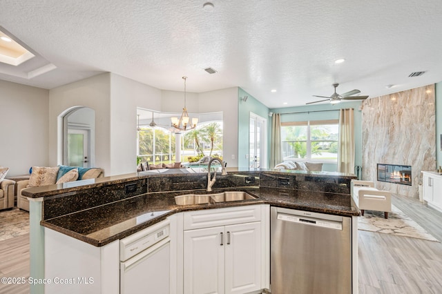 kitchen with open floor plan, dishwasher, a sink, light wood-style floors, and a textured ceiling