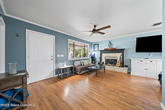 9633 Honeysuckle Dr, Sebastian, FL 32976 - living area featuring visible vents, crown molding, a ceiling fan, a glass covered fireplace, and light wood-style floors
