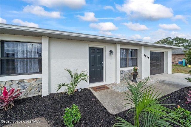 doorway to property featuring stucco siding, an attached garage, stone siding, and concrete driveway