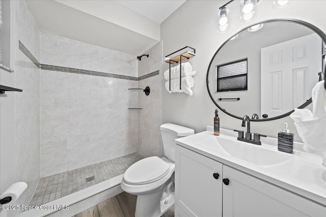 full bath with toilet, tiled shower, vanity, and wood finished floors