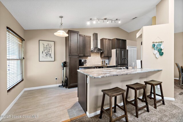 1265 Giralda Cir NW, Palm Bay, FL 32907 - kitchen with wall chimney range hood, a breakfast bar area, vaulted ceiling, freestanding refrigerator, and dark brown cabinetry