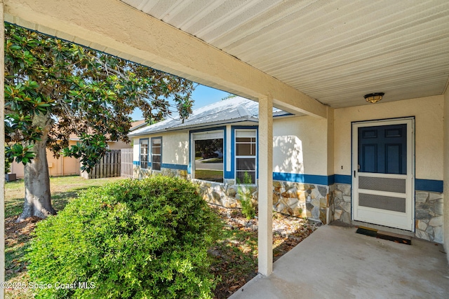 view of exterior entry with stone siding, stucco siding, and fence