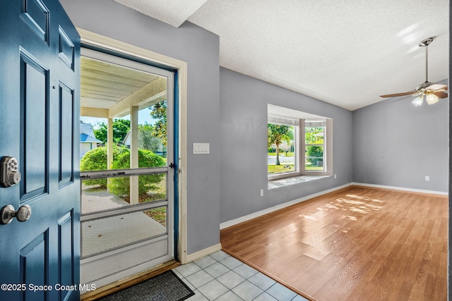 entryway with ceiling fan, vaulted ceiling, baseboards, light tile patterned floors, and a textured ceiling