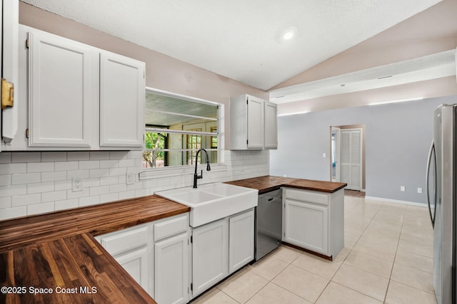 kitchen with wood counters, stainless steel appliances, a sink, decorative backsplash, and vaulted ceiling