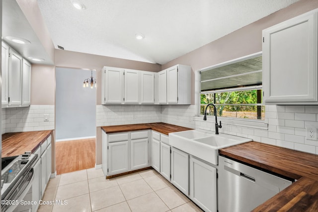 kitchen with butcher block counters, stainless steel appliances, a sink, decorative backsplash, and lofted ceiling