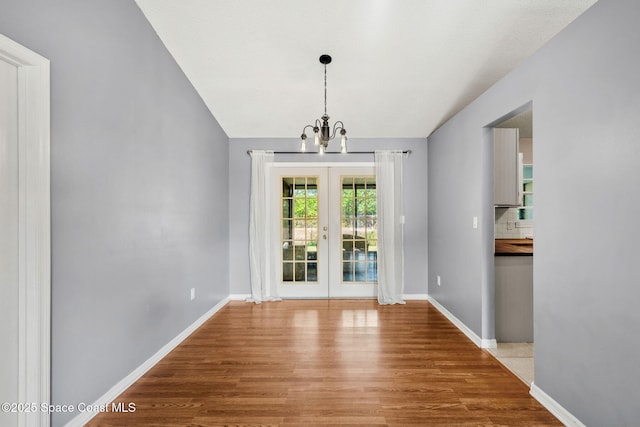 unfurnished dining area featuring french doors, a chandelier, wood finished floors, and baseboards