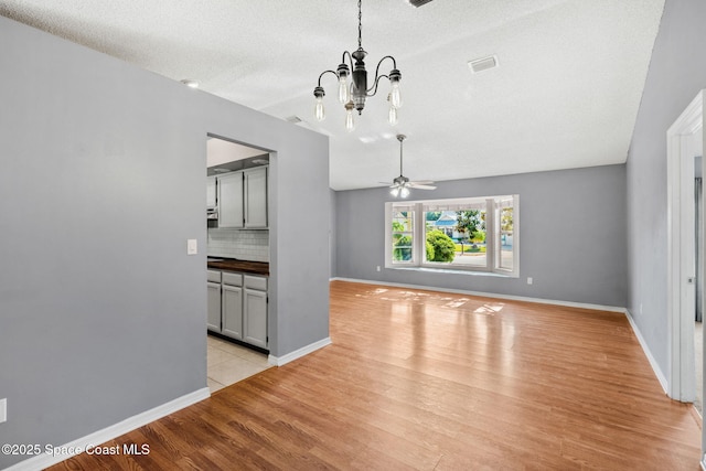 unfurnished dining area with light wood-type flooring, a chandelier, ceiling fan, baseboards, and a textured ceiling