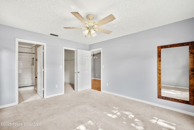unfurnished bedroom with carpet flooring, baseboards, a walk in closet, a textured ceiling, and ensuite bathroom
