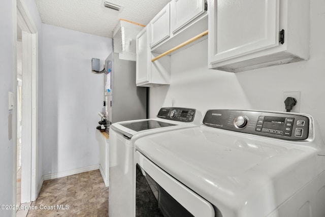 clothes washing area with washing machine and clothes dryer, baseboards, cabinet space, and a textured ceiling