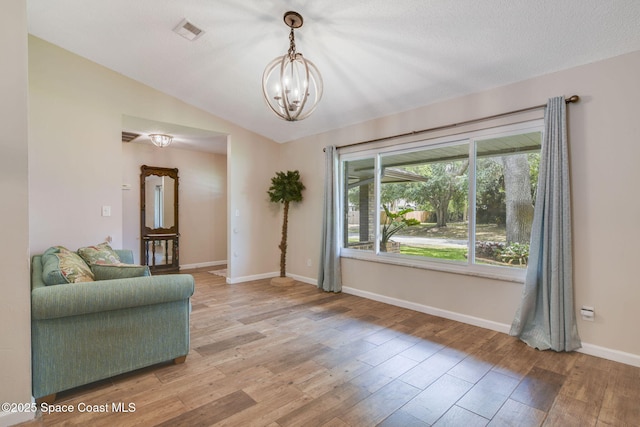 sitting room with a chandelier, light wood-type flooring, visible vents, baseboards, and vaulted ceiling