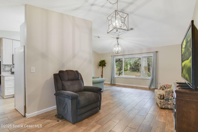 living area featuring lofted ceiling, a notable chandelier, baseboards, visible vents, and light wood-type flooring