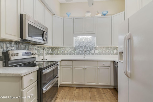 kitchen featuring a sink, stainless steel appliances, backsplash, light countertops, and light wood-style floors