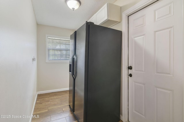 kitchen with baseboards, light wood finished floors, white cabinetry, and black fridge with ice dispenser
