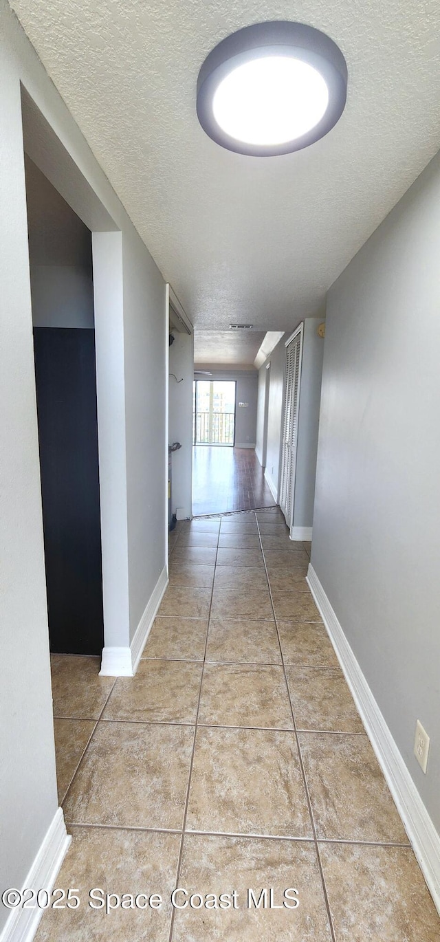 hallway with a textured ceiling, tile patterned floors, and baseboards