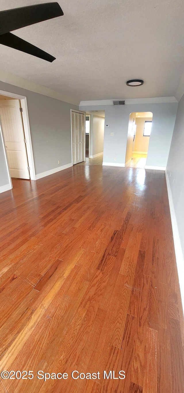 unfurnished room with wood finished floors, baseboards, and arched walkways