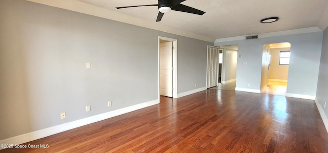 unfurnished room featuring arched walkways, a ceiling fan, wood finished floors, and baseboards