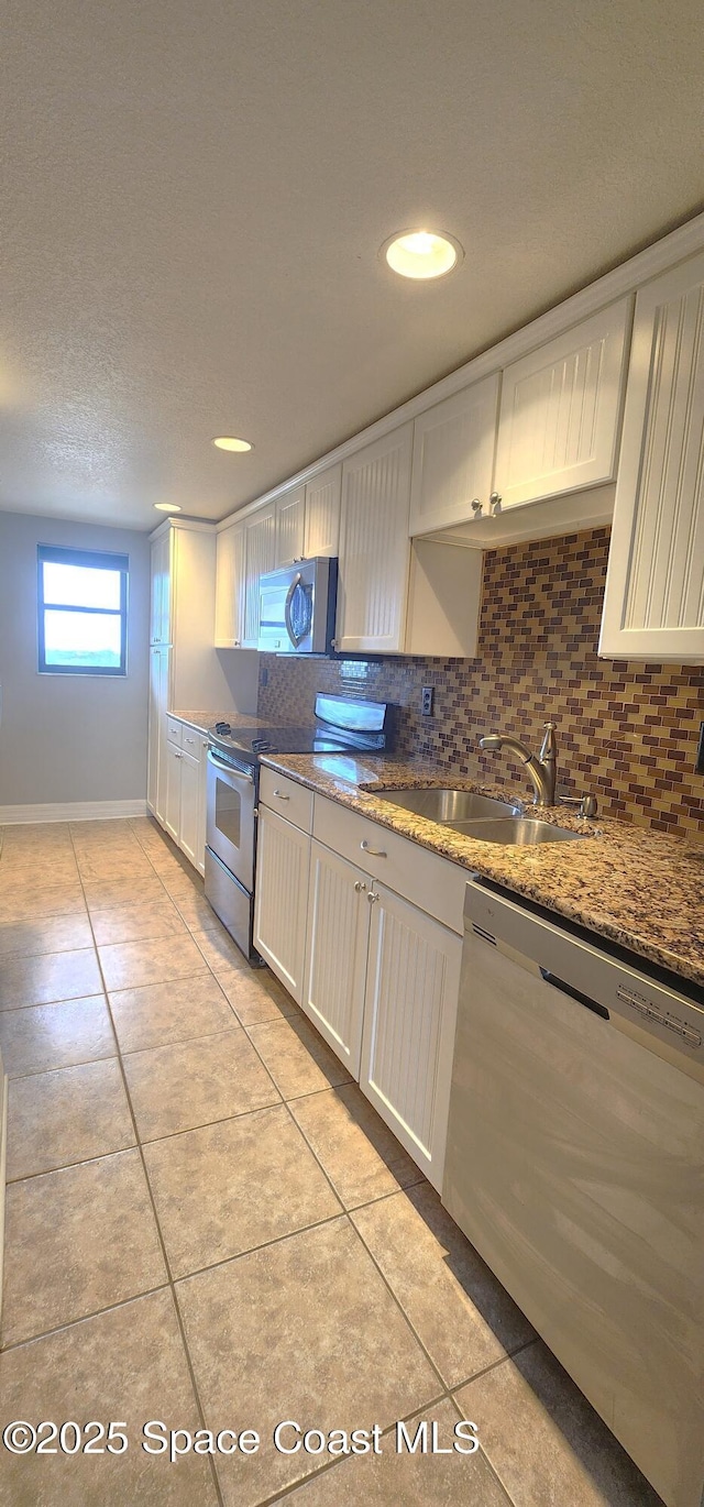 kitchen with appliances with stainless steel finishes, a sink, white cabinetry, light tile patterned flooring, and recessed lighting