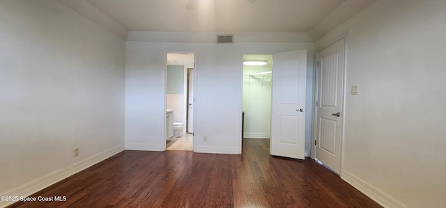 unfurnished bedroom with a spacious closet, wood finished floors, baseboards, a closet, and connected bathroom
