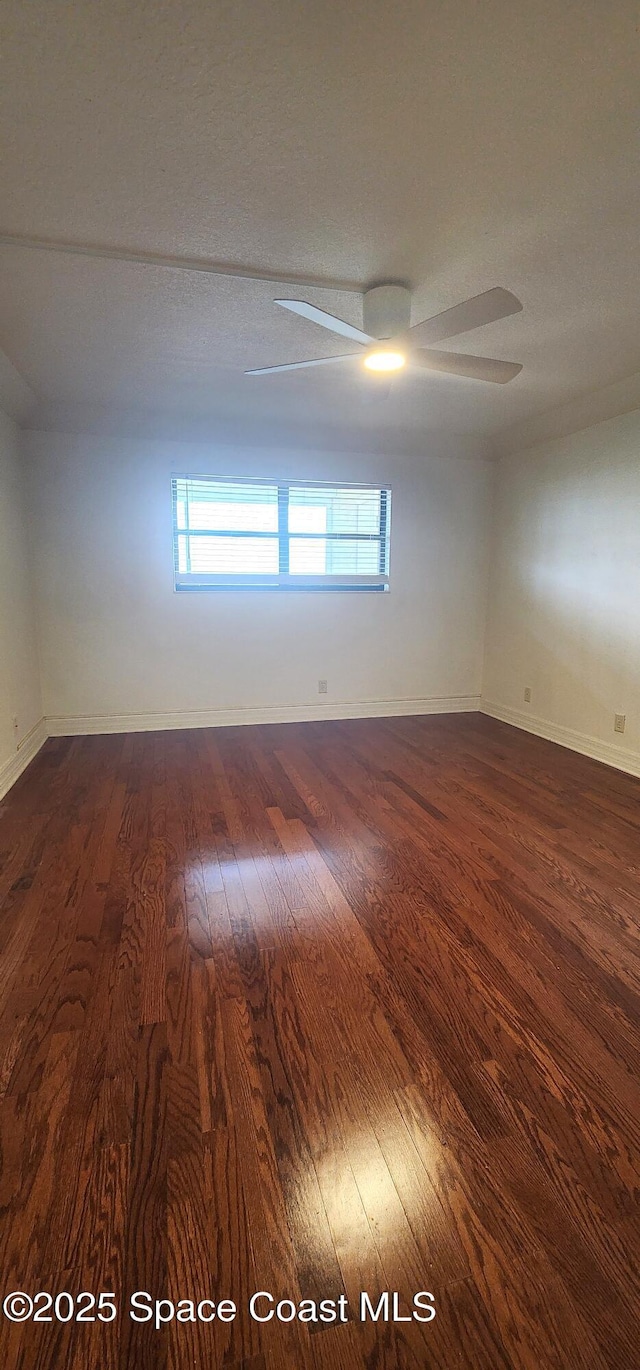 spare room featuring dark wood finished floors, a ceiling fan, and baseboards