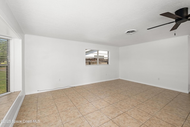 empty room with healthy amount of natural light, ceiling fan, light tile patterned floors, and a textured ceiling