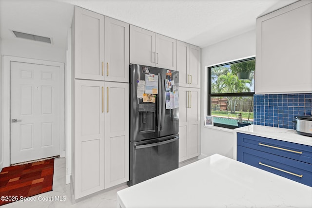 kitchen featuring fridge with ice dispenser, light countertops, light tile patterned flooring, decorative backsplash, and blue cabinetry