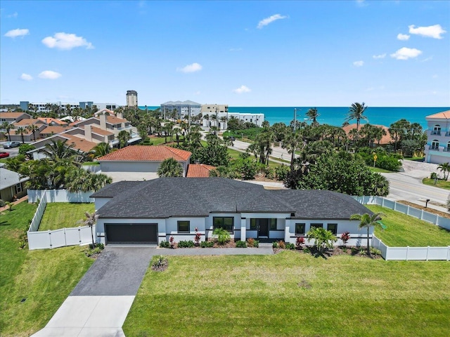 view of front facade featuring driveway, an attached garage, a water view, fence private yard, and a front lawn