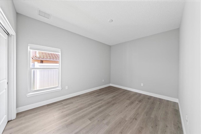 empty room with a textured ceiling, visible vents, wood finished floors, and baseboards