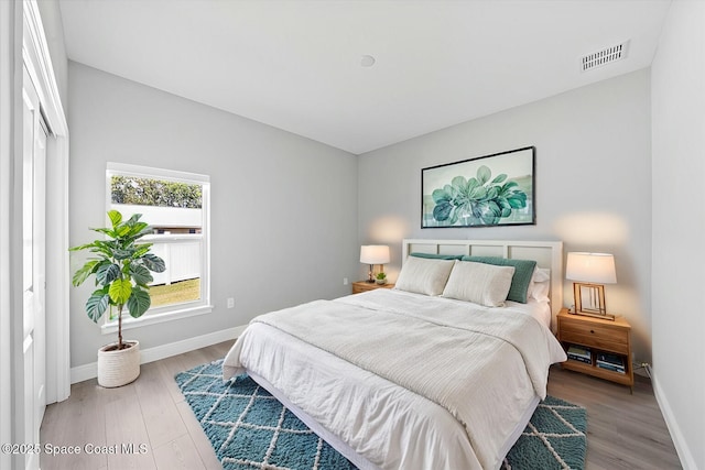 bedroom with baseboards, visible vents, and wood finished floors