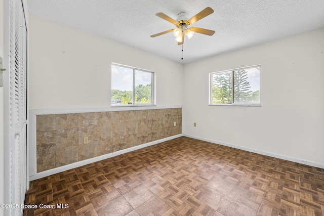 1554 Nona St NE, Palm Bay, FL 32907 - unfurnished room featuring plenty of natural light, a textured ceiling, a ceiling fan, baseboards, and a wainscoted wall