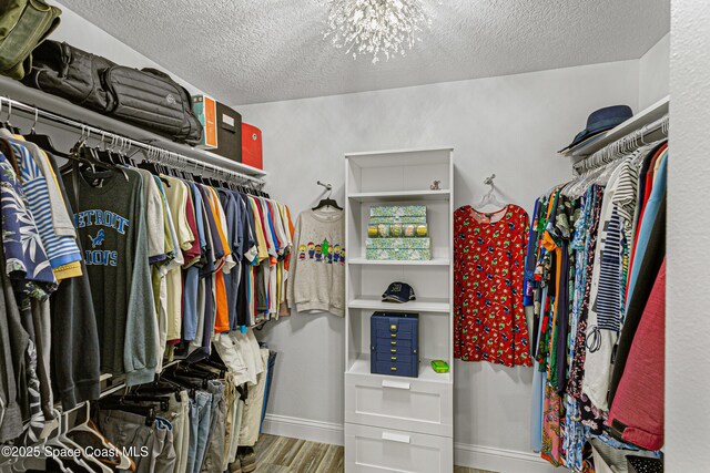 spacious closet featuring wood finished floors and a notable chandelier
