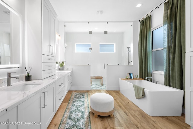 full bath with walk in shower, a sink, a freestanding bath, double vanity, and wood finished floors