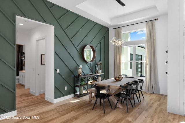 dining area with baseboards, light wood-style flooring, a chandelier, and a tray ceiling