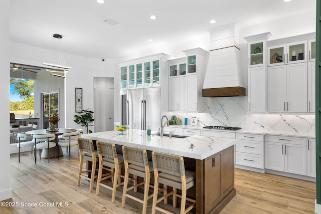 kitchen with high quality fridge, a sink, decorative backsplash, gas stovetop, and a center island with sink