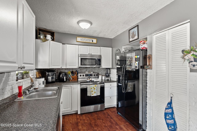 kitchen with appliances with stainless steel finishes, a sink, dark countertops, white cabinets, and decorative backsplash