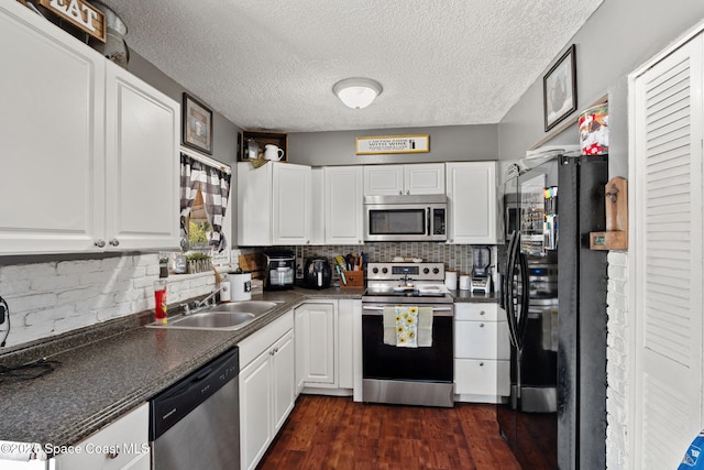kitchen with stainless steel appliances, a sink, dark countertops, white cabinetry, and a textured ceiling