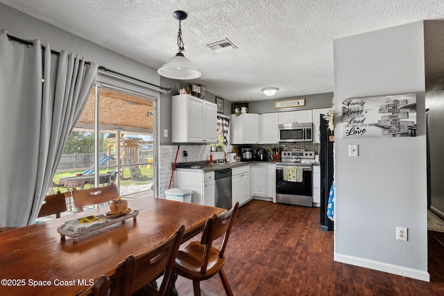 kitchen featuring appliances with stainless steel finishes, dark wood-type flooring, white cabinets, a sink, and decorative backsplash