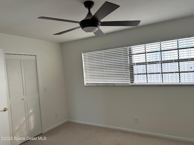 unfurnished bedroom featuring light colored carpet, a closet, baseboards, a ceiling fan, and multiple windows