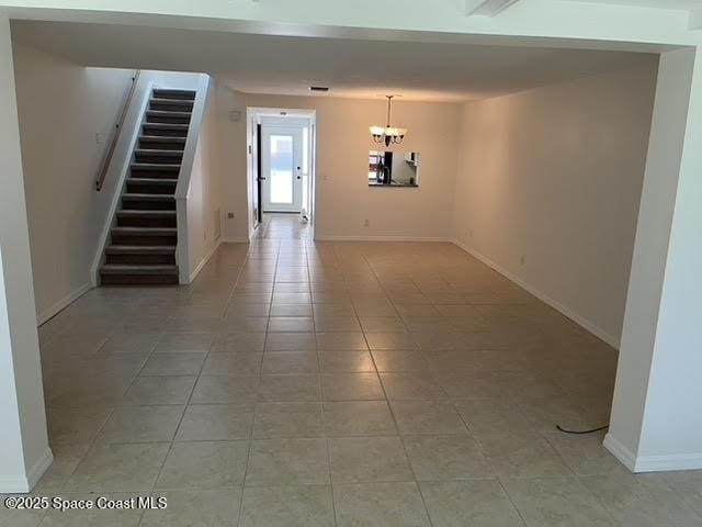 spare room with stairs, a chandelier, light tile patterned flooring, and baseboards