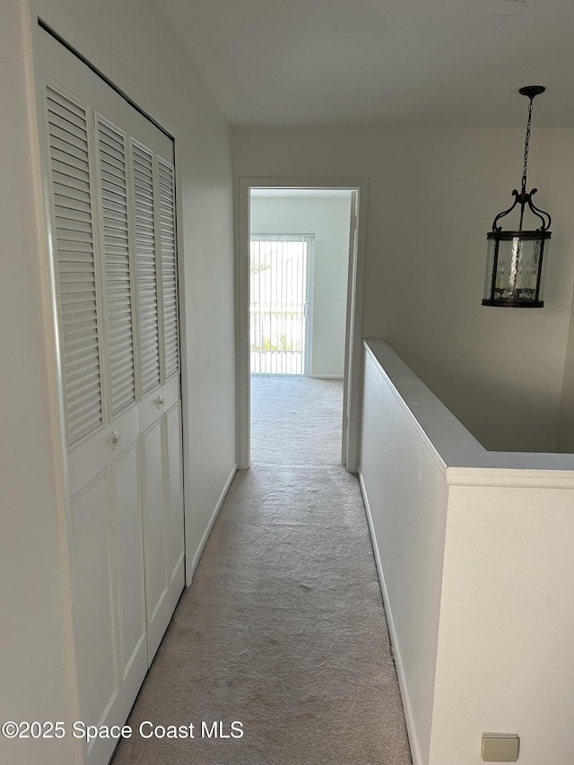 hallway featuring light colored carpet and baseboards
