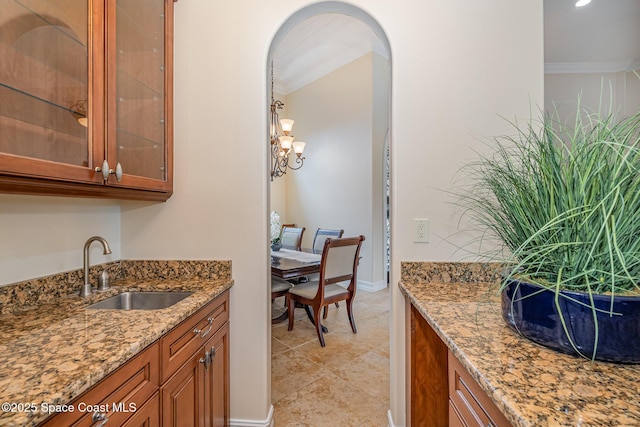 7346 Gorda Peak Ct, Melbourne, FL 32940 - kitchen with brown cabinets, a sink, light stone counters, glass insert cabinets, and ornamental molding