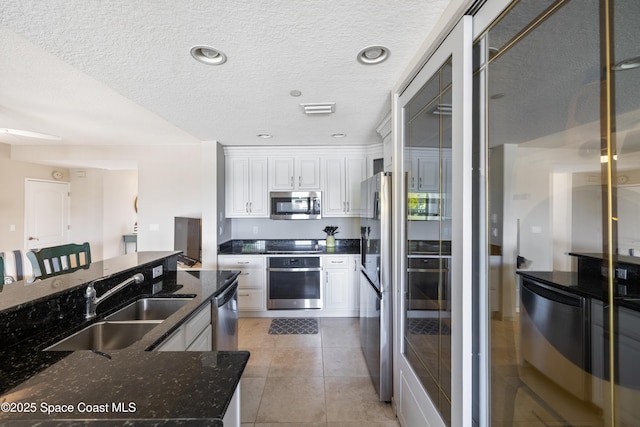 kitchen with dark stone countertops, a sink, stainless steel appliances, white cabinets, and a textured ceiling