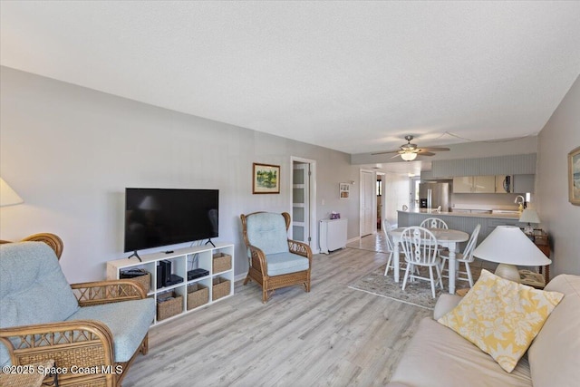 living area featuring light wood-style floors, baseboards, a ceiling fan, and a textured ceiling