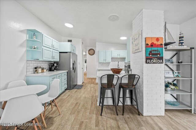 215 Jefferson Ave, Cape Canaveral, FL 32920 - kitchen featuring stainless steel refrigerator with ice dispenser, blue cabinets, open shelves, and decorative backsplash