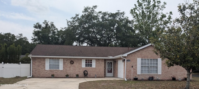 ranch-style house featuring concrete driveway, fence, a garage, brick siding, and roof with shingles